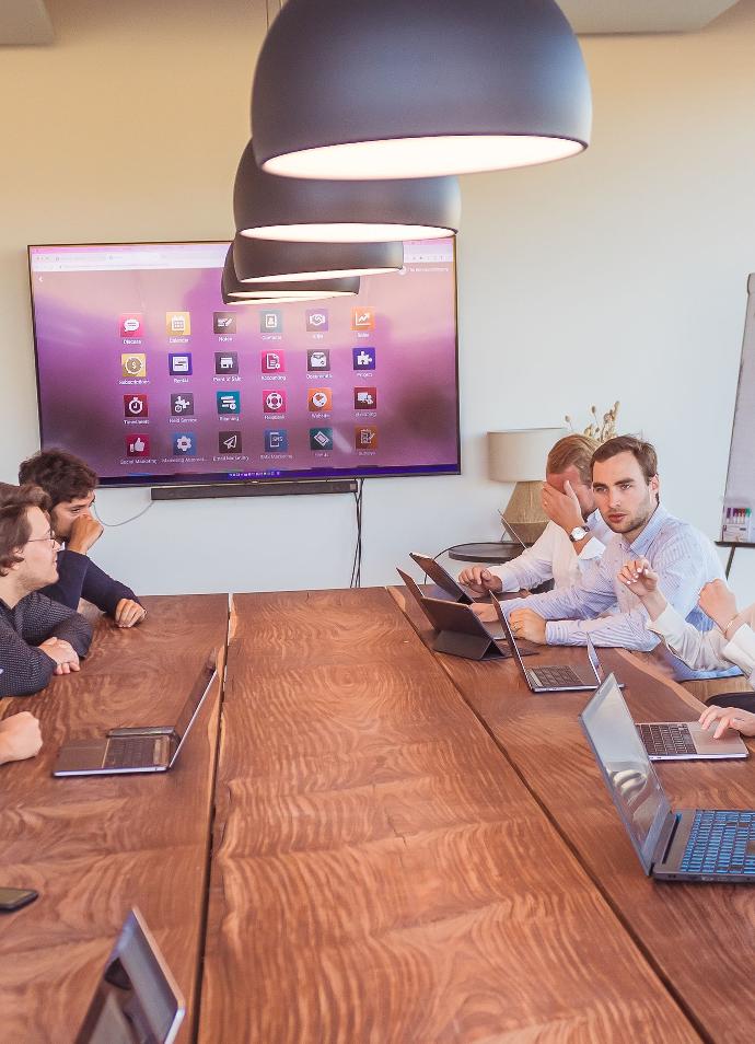 todo el equipo de la empresa de servicios alrededor de una mesa con muchos portátiles y una pantalla en la que se muestran todas las aplicaciones de Odoo