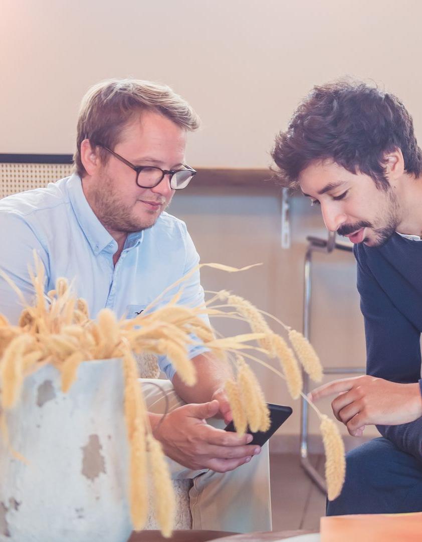 foto van Ilias Bitar en Brieuc Thoumsin bespreken uw digitale potentieel met de hulp van onze experts rond een mobiele telefoon zittend op stoelen met een mooie plant op de voorgrond