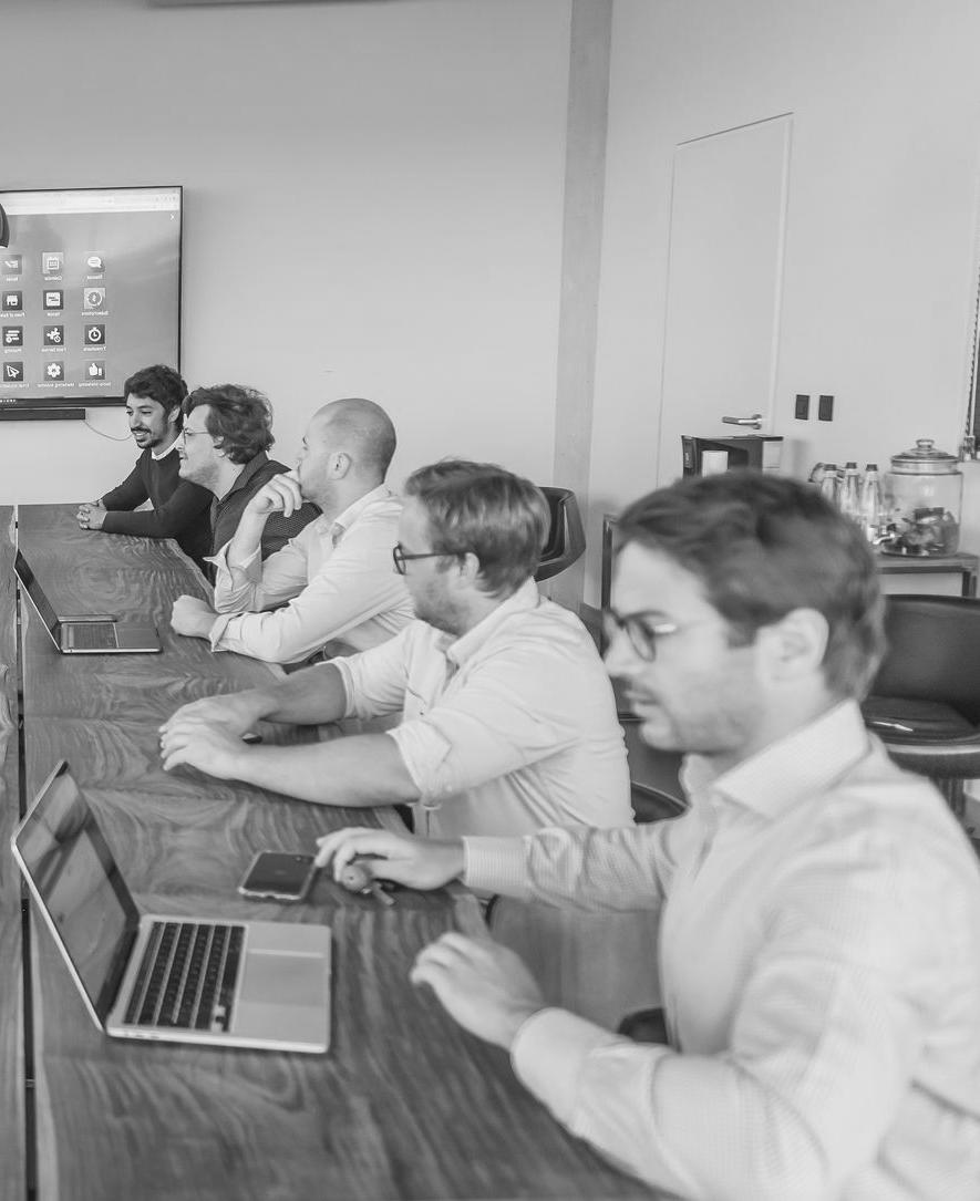 les hommes de the service company autour d'une table comprenant Valery Jans, Brieuc Thoumsin et Ilias Bitar munis de leur ordinateur portable et téléphone portable ainsi qu'un écran qui affiche toutes les applications Odoo, Nos valeurs Respect, intégrité et résultats