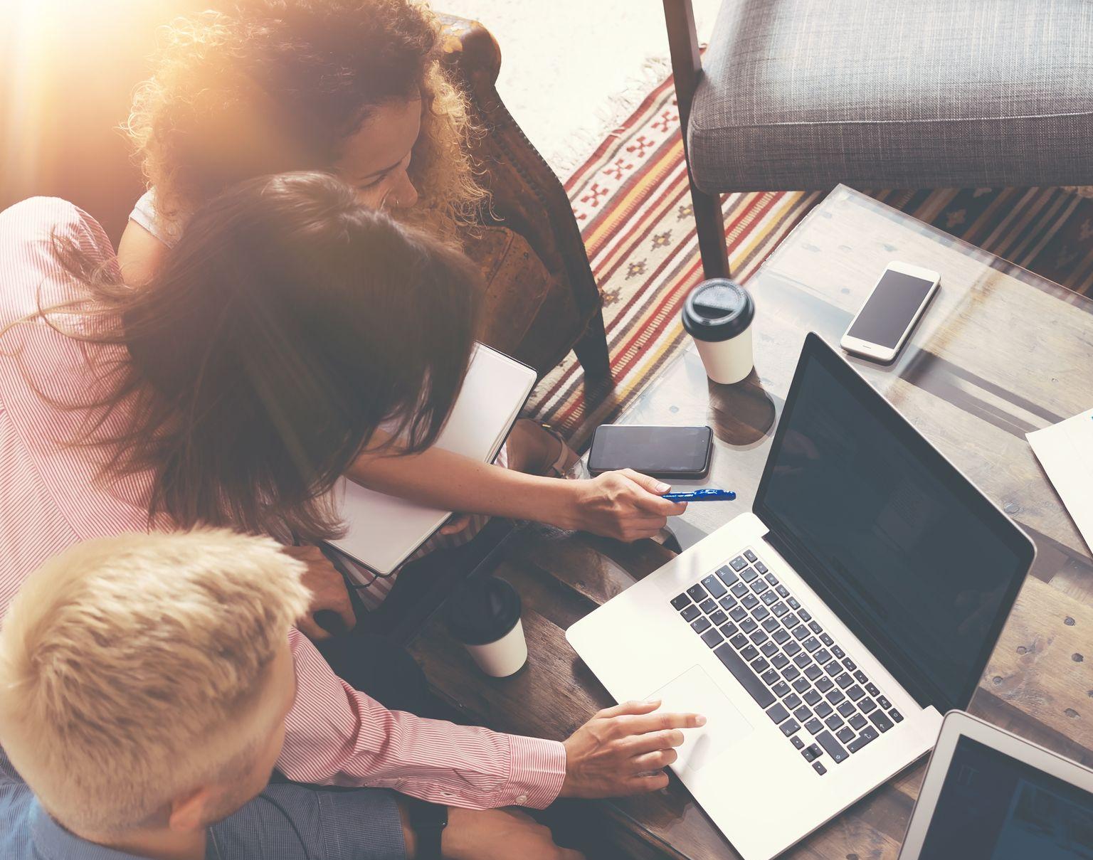 three people around a laptop talking about the 2021 digital marketing guide for SMEs, there are also mobile phones as well as a cup of coffee and a notepad